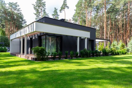 Realizacja nowoczesnego domu parterowego z ciemną elewacją, białym zadaszeniem tarasu i dużym ogrodem, przykład projektu typu HomeKONCEPT wybudowanego przez New-House.